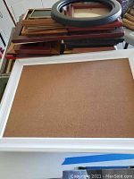 View of assorted stacked picture frames including large white corkboard frame