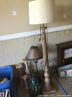 Photo showing tall lamp with beige fabric shade, wooden carved base and three pastel wooden candle holders