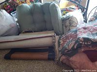 Photo of rolled throw rugs, pink quilted items, and cushions with floral patterns stacked on floor.