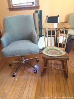 Both chairs side by side in a room with hardwood floor. Office chair is gray with metal base and wheels; rocking chair is wooden with a round braided seat pad, showing some wear and wobble.
