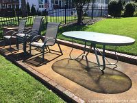 Side view of five metal mesh chairs and oval glass top patio table on paved surface outdoors in sunlight