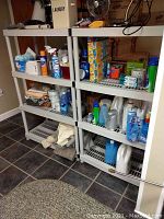 Frontal view showing two plastic shelving units filled with various household items (not included in sale) in a basement room with tiled floor.