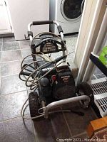 Front angle view of Honda GC 160 pressure washer showing engine, frame, hoses wrapped around and wheels.