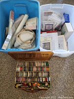 Two large plastic bins with fabric swatches, cross-stitch patterns, printed charts, and various supplies.