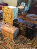Side table with drawer and cabinet and two trunks; table painted light yellow with butterflies, trunks positioned in front.