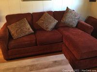Front view of red Clayton Marcus sofa with attached chaise and three paisley throw pillows arranged on seat and chaise.