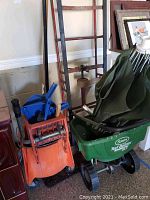 Photo showing Scotts Turf Builder spreader, green mop bucket holding cleaning tools, orange furniture mover behind, broom visible to side