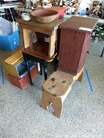 Photo showing wooden stools, a red-brown cabinet, one large wooden bowl on one stool, and another smaller wooden bowl beneath the large bowl.