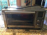 Full view of toaster oven showing stainless steel body, glass door with metal handle, and power cord on top.