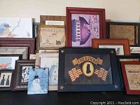 Multiple framed prints and plaques stacked against a wall, featuring patriotic and nature themes, showing size and composition of items in the lot.