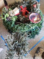 Photo showing multiple artificial holiday wreaths with lights, red bows, succulents, and Christmas ornaments loosely stacked.