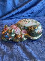 Side view of antique porcelain sleeping cat figurine with floral and gilt detailing on a fabric backdrop