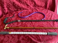 Photo showing all three items side by side on a red floral fabric background: brass handled wooden cane, green Backnobber II cane massager, and purple The Stick muscle massager.