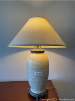 Full view of the lamp showing the ceramic urn body, off-white linen shade, and metal base.