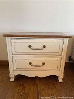 Front view of nightstand showing antiqued white distressed finish with two drawers and decorative handles.