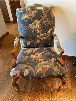 Front view of the tapestry and wood arm chair showing overall upholstery pattern and carved frame.