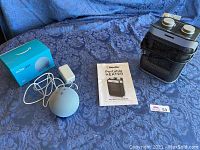 Photo showing Amazon Echo Dot with box and Mueller portable heater with instruction manual on blue textile surface.