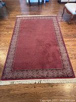 Full view of the wool Persian style rug, deep red with patterned border and fringe on ends.