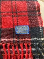 Close-up of Pendleton label on red and black wool tartan throw blanket showing 100% pure virgin wool and Made in USA.