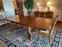 Wide shot showing Mt. Airy trestle dining table with one leaf extended and 6 dining chairs arranged around it on floral patterned rug.