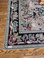 Close-up view of the rug's floral and leaf border design with black background and rose/sage accents.