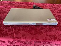 Phillips DVD player in silver color shown on a red patterned cloth surface.