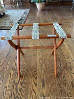 Full view of the wood luggage stand on hardwood floor showing cream and green tapestry straps and overall structure