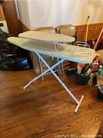 Standard size ironing board with metal rack, shown set up on floor, missing two rubber feet but stable