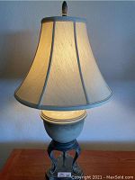 Full view of urn style lamp illuminated showing bell-shaped shade and urn shaped body.