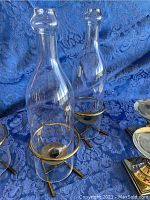4 glass hurricane candle holders with brass rims and wicker handles on blue fabric background