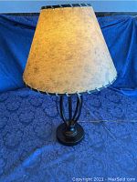 Full view of the vintage bronze metal lamp with antique style paper shade on blue fabric background.