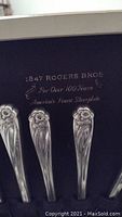 Close-up of silverware handles showing '1847 Rogers Bros' and floral pattern on silverplate handles, along with presentation box interior.