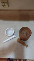 Marble mortar and pestle set with white polished finish next to wooden mortar and pestle with natural wood grain, showing both items separately.