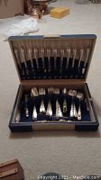 Full view of the antique silverware set within blue velvet and tan satin lined storage case.