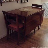 Angle view showing drop leaf table folded on sides with two chairs tucked under one side.