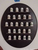 Full view of all 20 bird illustrated ceramic thimbles arranged on the dark wooden semi-circular shelf.