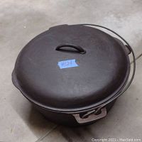 Top view of the well-seasoned cast iron Dutch oven with domed lid and bail handle, showing a blue label #124.