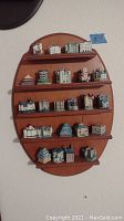 Wall mounted wooden oval shelf with four horizontal tiers holding 20 miniature castle thimbles. Shelf surface has minor scratches visible.