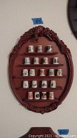 Full view of oval carved wooden wall shelf with cat figure displaying 21 thimbles arranged evenly on five shelves