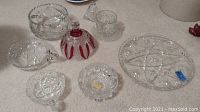 Various crystal glassware items including bowls, plates, an inkwell with red accents, and ashtrays arranged on a surface.