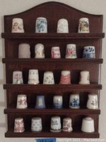 Wooden display shelf with 23 flower-decorated ceramic thimbles arranged on four rows