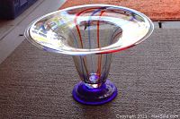 Side view of hand blown glass bowl showing flared rim, clear glass with blue/red swirls, and blue circular base