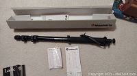 Manfrotto monopod fully extended next to original box and instruction manuals, placed on carpeted floor.
