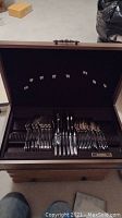 Wooden hinged box holding the full silverware set organized by type.