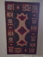 Full view of the colorful handmade antique tapestry hung vertically, showing central geometric pattern and border with floral and leaf motifs.