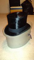 Black top hat on protective gray case side view, showing height and glossy texture of the hat