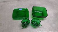 Four pieces of vintage Forest Green glassware including two square bowls and two cups with handles shown in green translucent glass.