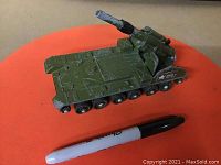 Dark green diecast Chieftain tank model with visible paint wear and white military star insignia on side, placed on orange surface with pen for scale.