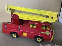 Side view of red metal toy truck with yellow plastic bucket arm lifted, showing condition and design.