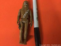 Front view of vintage Chewbacca action figure showing full body and blaster held in hand, alongside a pen for scale comparison.